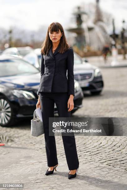 Guest wears a blazer jacket, suit pants, black pointy shoes, a Dior gray bag, outside Dior, during Paris Fashion Week - Womenswear Fall/Winter...