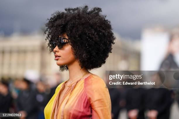 Guest wears Dior sunglasss, a yellow and pink pleated dress, outside Dior, during Paris Fashion Week - Womenswear Fall/Winter 2020/2021, on February...