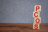 Abbreviation PCOS (polycystic ovarian syndrome) text acronym on wooden cubes on dark wooden backround. Medicine concept.