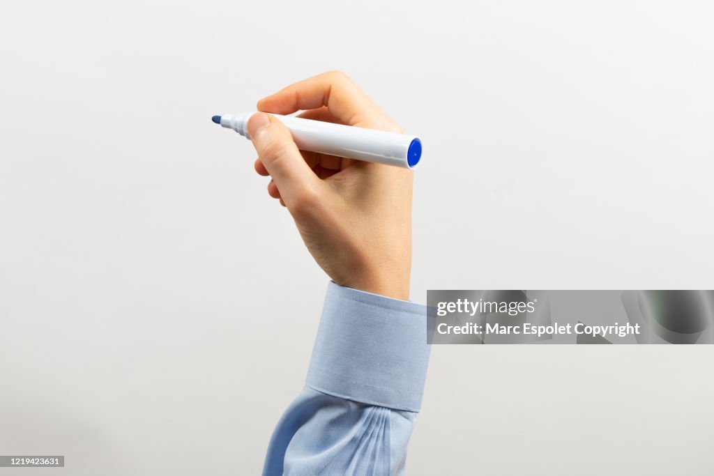 Rised arm writing with a blue marker in a transparent white board