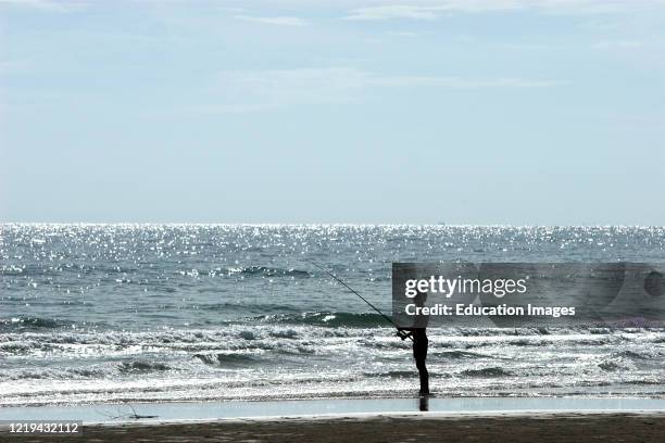 Man fishing with rod at water edge beach Ko Chang Thailand.