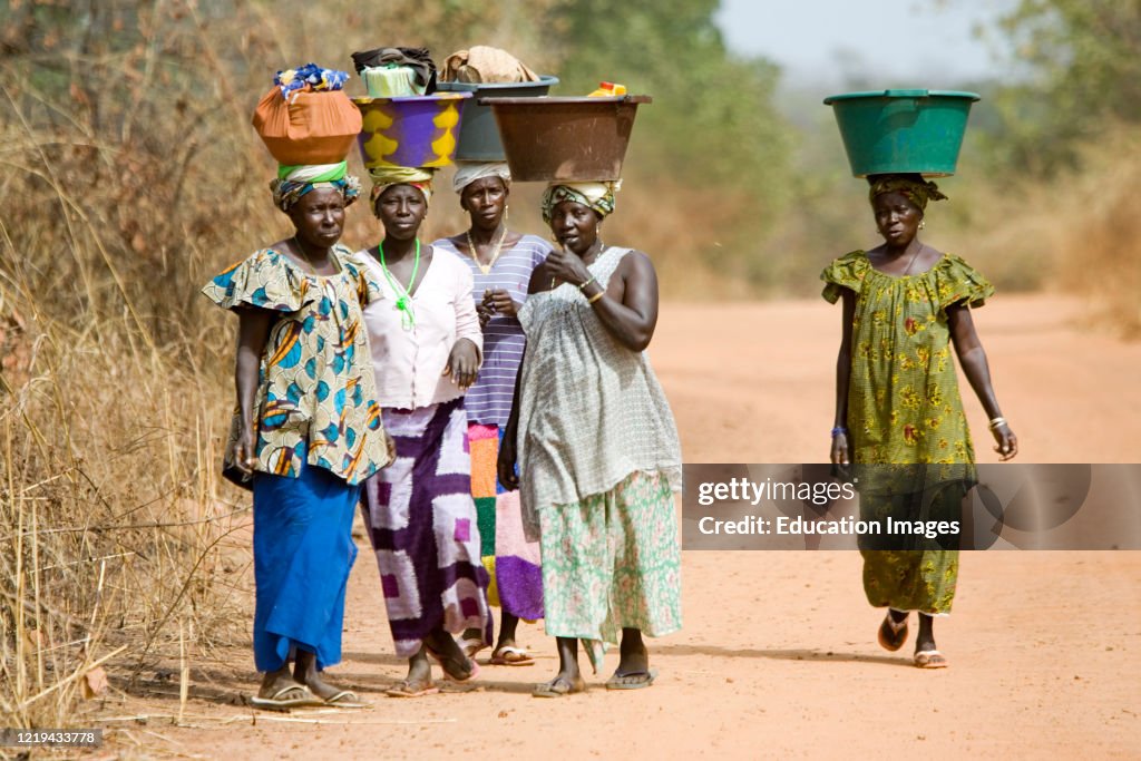 Women carry large colored basins and goods on head bush road The Gambia