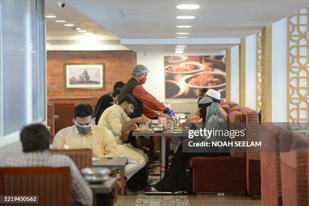 Waiter serves biryani rice to customers, while following social distancing guidelines at Paradise restaurant on the first day of its opening after...