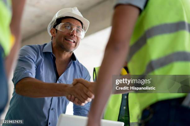 fröhlicher schiedsrichter, der einen bauunternehmer auf einer baustelle mit der hand schüttelt - building partnership stock-fotos und bilder