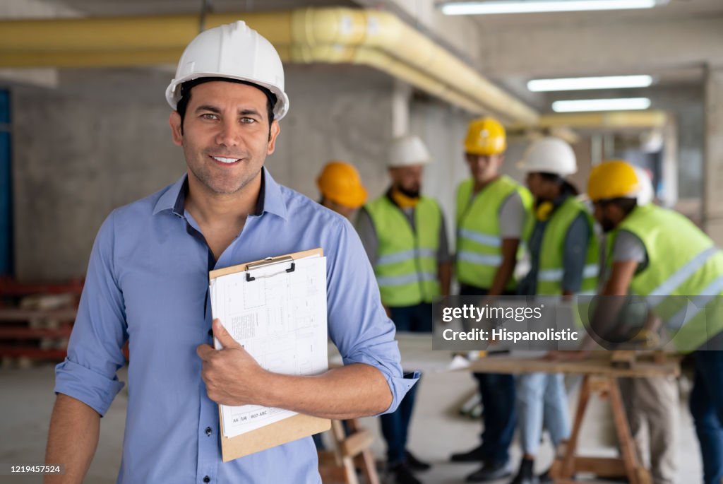Retrato de arquiteto alegre em um canteiro de obras segurando uma prancheta sorrindo para a câmera
