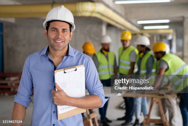 portrait of cheerful architect at a construction site holding a clipboard smiling at camera - engenheiro civil imagens e fotografias de stock