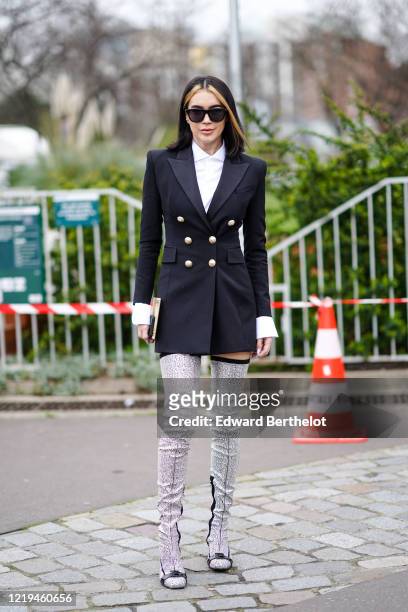 Brittany Xavier wears sunglasses, a white shirt, a black double-breasted jacket with brass buttons and padded shoulders, glittering bejeweled Balmain...