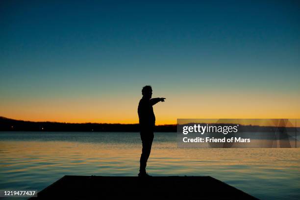 silhouette full length of man pointing at lake in early morning with blue gradient sky - seeufer stock-fotos und bilder