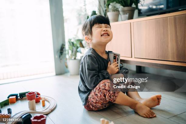 cute little asian girl receiving a gift from her parents, hugging the gift and smiling joyfully in the living room at home - unexpected stock pictures, royalty-free photos & images