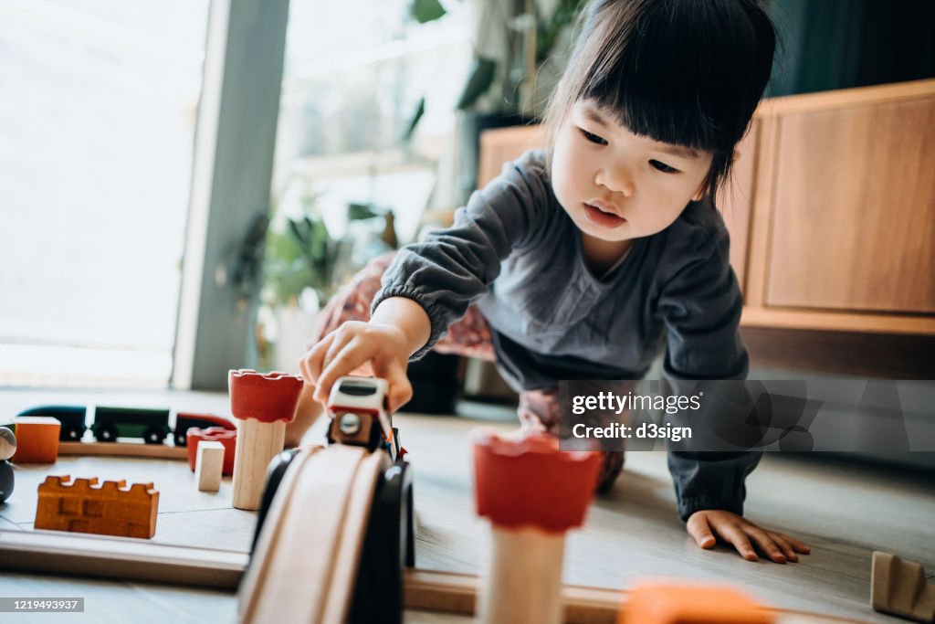 Cute little Asian girl playing with wooden toy train in the living room at home