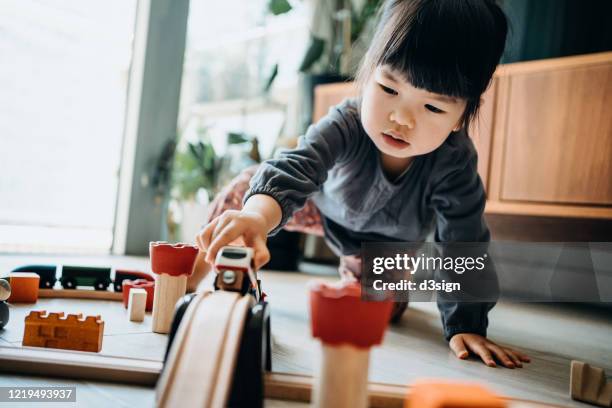 cute little asian girl playing with wooden toy train in the living room at home - asian toddler stock pictures, royalty-free photos & images