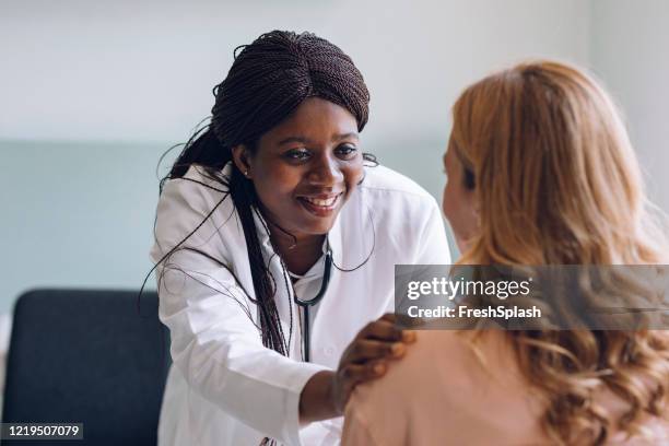 care and compassion and trust: smiling doctor lays her hand on the patient's shoulder - patience office stock pictures, royalty-free photos & images