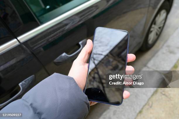 locating the car using a mobile application with gps. man's hand holding a mobile phone in front of a car.  berlin. germany. - car keys hand stockfoto's en -beelden
