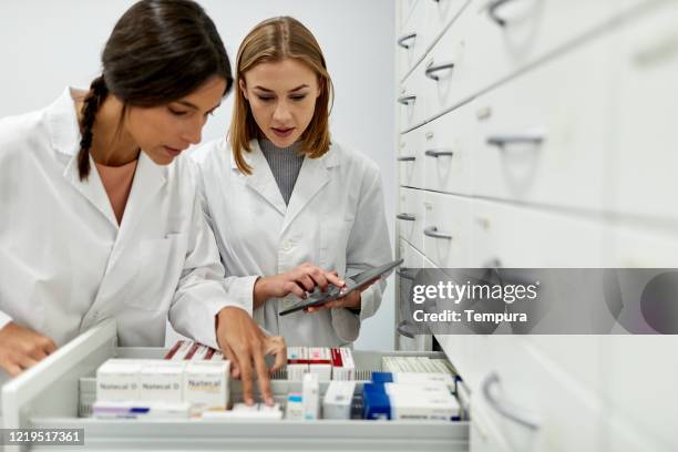 zwei apothekerinnen sortieren medikamente im lagerbereich. - schrank stock-fotos und bilder