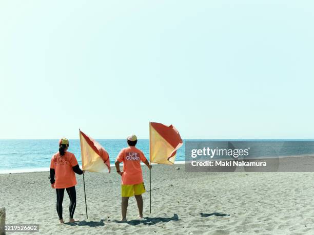 female life saver standing towards the sea with flag in hand. - chigasaki 個照片及圖片檔