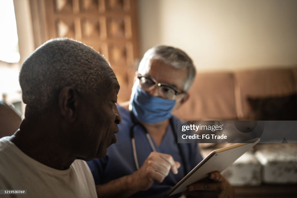 Health visitor and a senior man during home visit - using digital tablet
