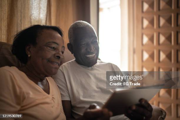 pareja de la tercera edad en una videollamada usando una tableta digital en casa - lovers 2020 film fotografías e imágenes de stock