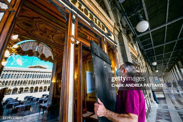An employee takes off wooden shutters from the facade of 18th Century Cafe Florian on June 12, 2020 on St. Mark's Square in Venice, which reopens...