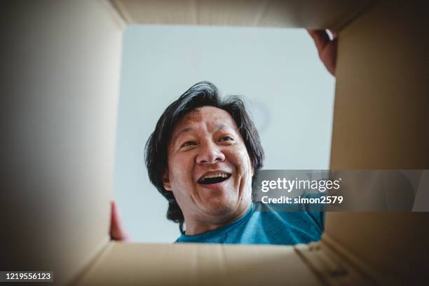 asian man surprised is looking inside cardboard box - caixa aberta imagens e fotografias de stock