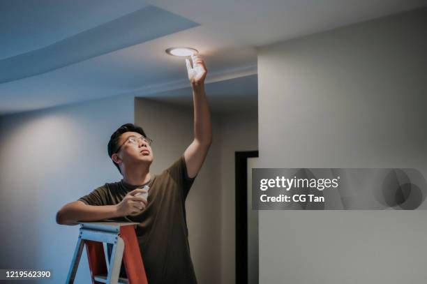 un maschio asiatico cinese medio adulto che cambia lampadina in soggiorno, casa appartamento - luce led foto e immagini stock