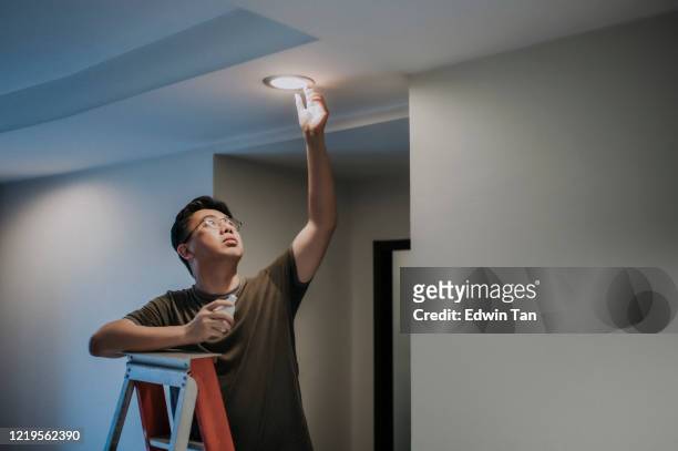 アジアの中年成人男性は、リビングルーム、アパートの家で電球を交換 - led ストックフォトと画像