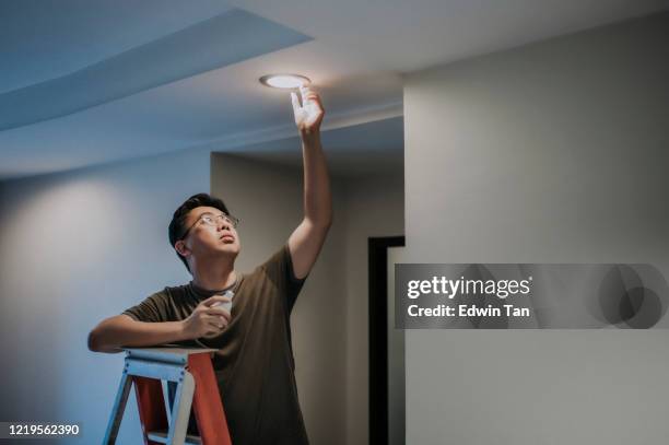 an asian chinese mid adult male changing light bulb in living room, apartment home - leds stock pictures, royalty-free photos & images