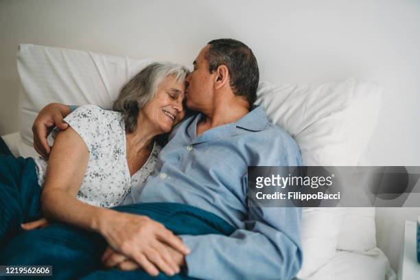 mature couple in bed together. man kissing the forehead of his wife - good morning kiss images stock pictures, royalty-free photos & images