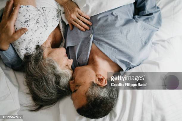 high angle view of a mature couple in bed together. man kissing the forehead of his wife - good morning kiss images stock pictures, royalty-free photos & images