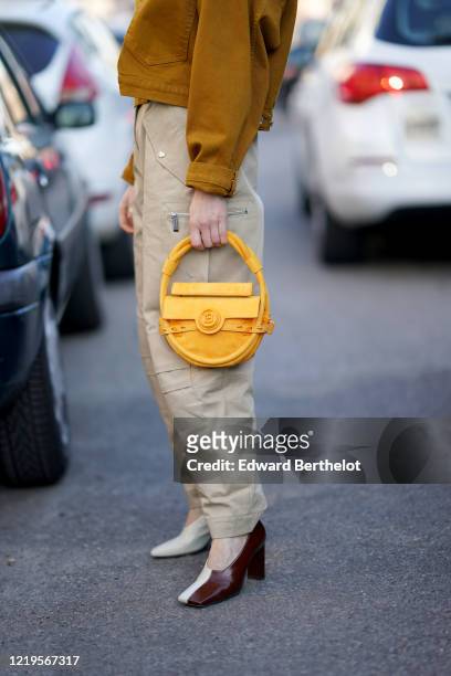 Julia Comil wears a brown/orange suede jacket, a yellow Balmain bag, gray pants, brown and white leather pointy shoes, outside Marni, during Milan...