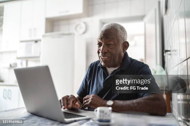 uomo anziano che lavora al laptop a casa - terza età foto e immagini stock