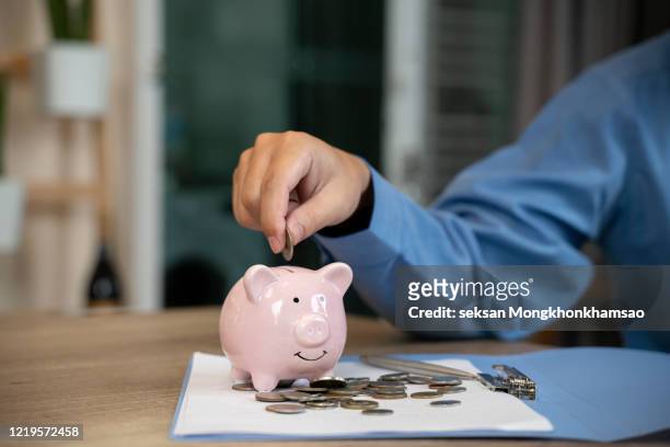 man putting a coin into a pink piggy bank concept for savings and finance - british coin stock pictures, royalty-free photos & images