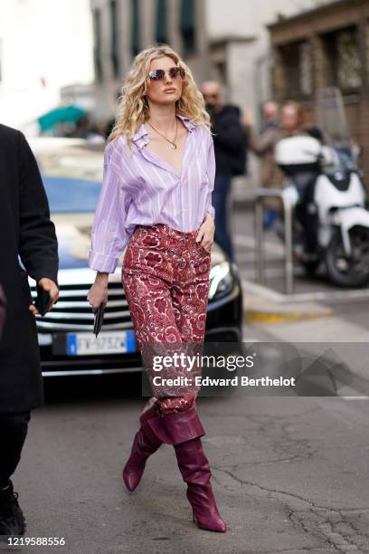 Romee Strijd wears a mauve pale purple shirt, a golden necklace, red pants with floral print, purple leather pointy boots, outside Etro, during Milan...