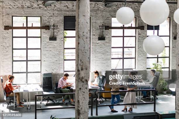 modern companies: group of young business people at a spacious loft open space coworking office working together - wide angle stock pictures, royalty-free photos & images