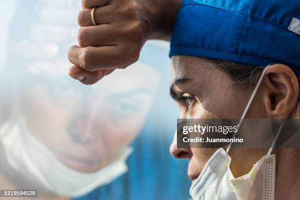 travailleur de la santé surmené regardant par une fenêtre, très préoccupé, très fatigué - crouler sous le travail photos et images de collection