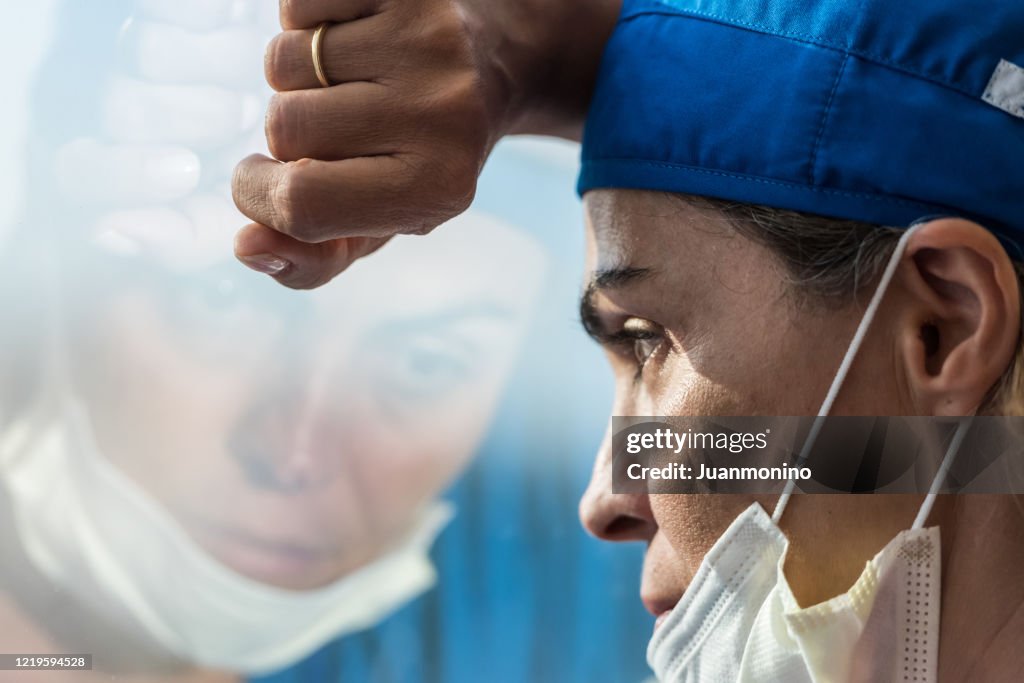 Overworked healthcare worker looking through a window, very concerned, very tired