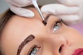 Close-up Photo of Beautician Applying Dye on Woman's Eyebrows - stock photo