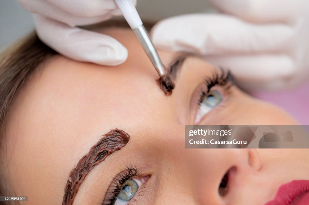 Close-up Photo of Beautician Applying Dye on Woman's Eyebrows - stock photo