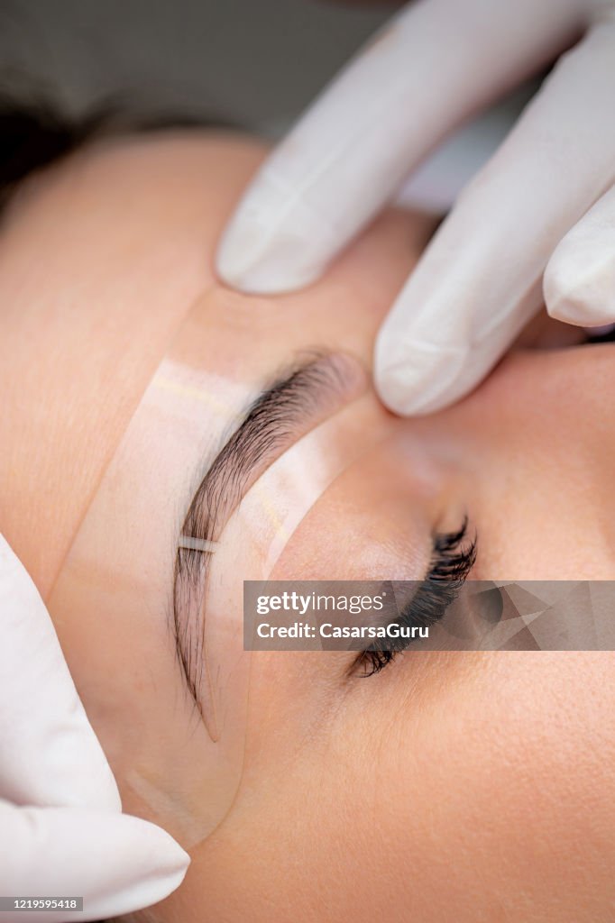 Beautician Using Transparent Stencil to Perfectly Shape Customer's Eyebrows - stock photo