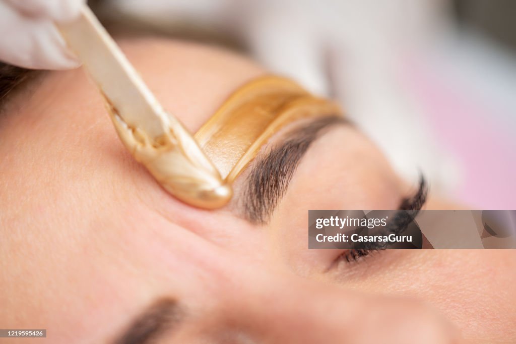 Applying Gold Colored Wax with Spatula on Woman's Face - stock photo
