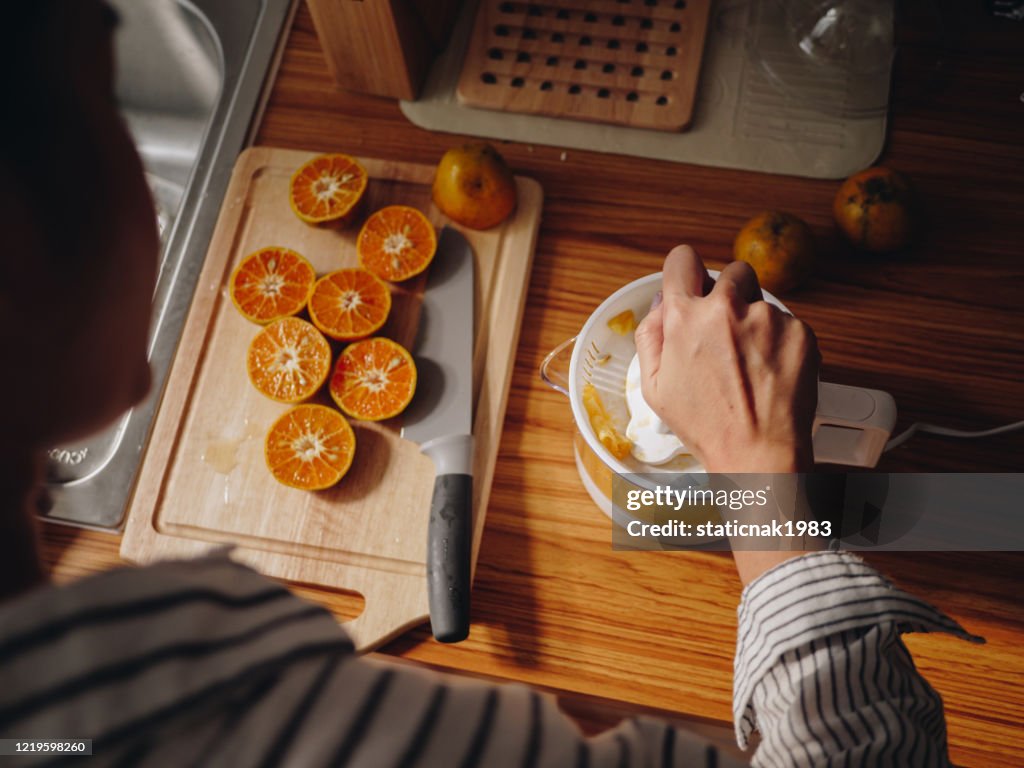 Mujer joven exprimiendo naranja con máquina exprimidora en el mostrador de la cocina