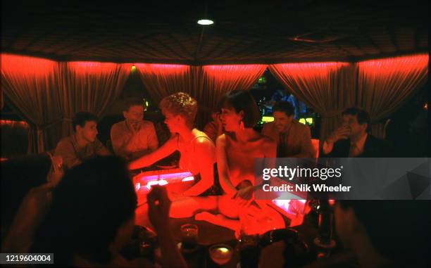 Topless barmaids sit inside circular bar serving drinks to patrons at the cocktail lounge "Bottoms Up" in Kowloon in 1980s;