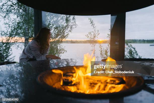 woman sitting near campfire in glass garden house at the evening - metal grate stock pictures, royalty-free photos & images