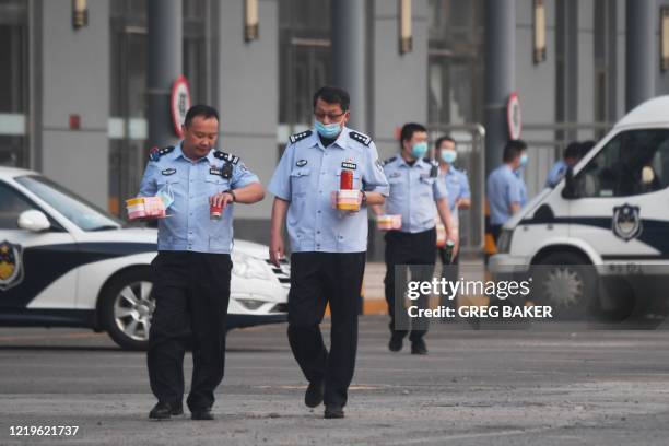 Police officers carry food as they walk in the grounds of a closed bus station near the closed Xinfadi market in Beijing on June 13, 2020. - The huge...
