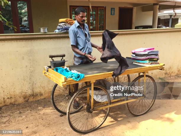 Man using a cart serving as an ironing board as he irons clothes for homeowners with a coal powered iron along a in Thrikkannapuram,...