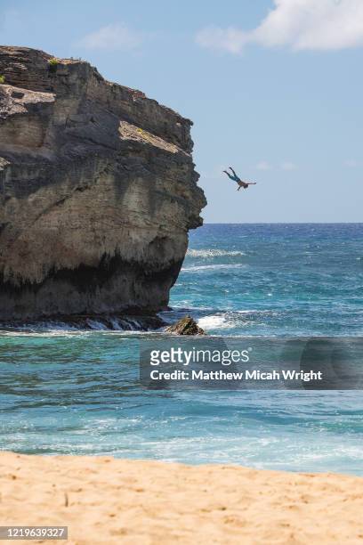 a man jumps off a 40 foot cliff at shipwreck's beach, kauai. - jumping into water stock pictures, royalty-free photos & images