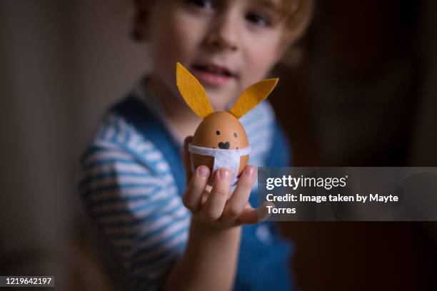boy holding and showing easter eggs wearing a surgical mask and looking at camera - doll fotografías e imágenes de stock