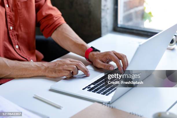 manos de un empresario anónimo con una camisa roja escribiendo en un ordenador portátil - reds fotografías e imágenes de stock