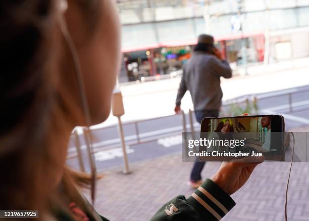 Japanese woman Noemi poses for a picture as she watches on her smartphone the live stream performance of Billie Eilish and Finneas O'Connell during...