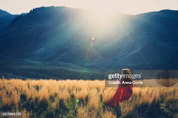 back view of woman in red cape running through golden field at sunset toward shadowed hills, sunbeam effect - runaway 個照片及圖片檔