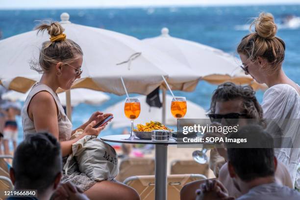 Two people are seen having an aperitif on one of the terraces of the Mar Bella beach bar. First weekend of bathing on the beaches of Barcelona with...